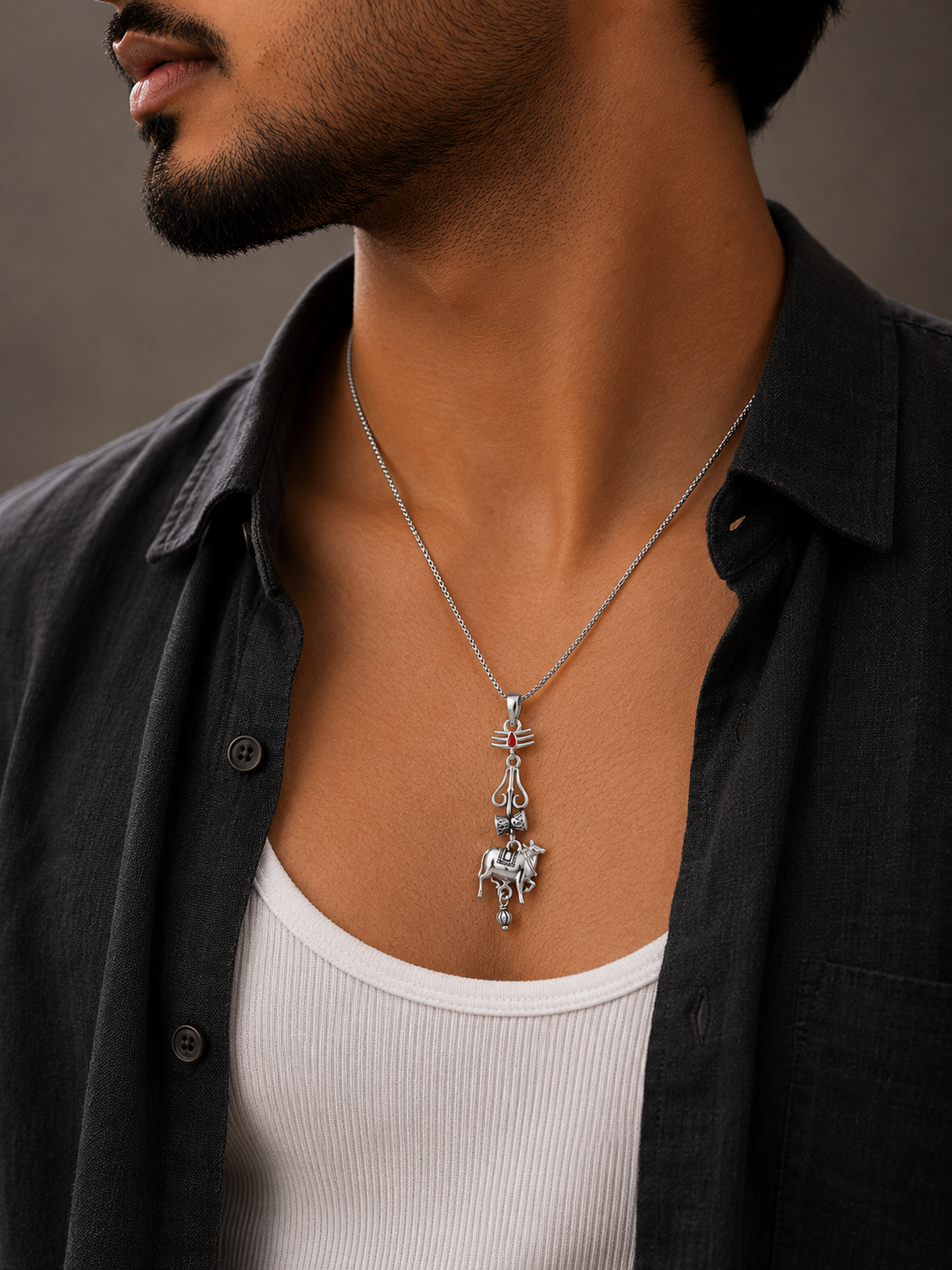 Man wearing a black shirt and white tank top with a silver necklace featuring a ssmb varanasi pendant.