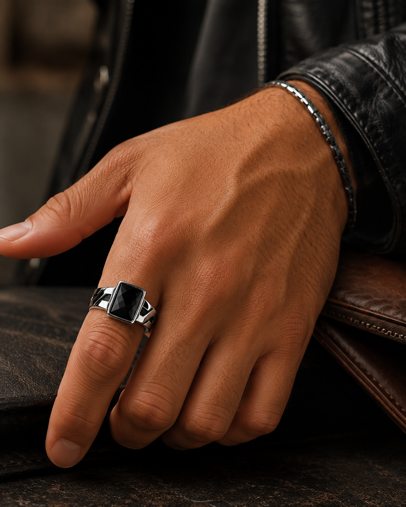 Hand wearing a black ring with a silver band on a leather surface
