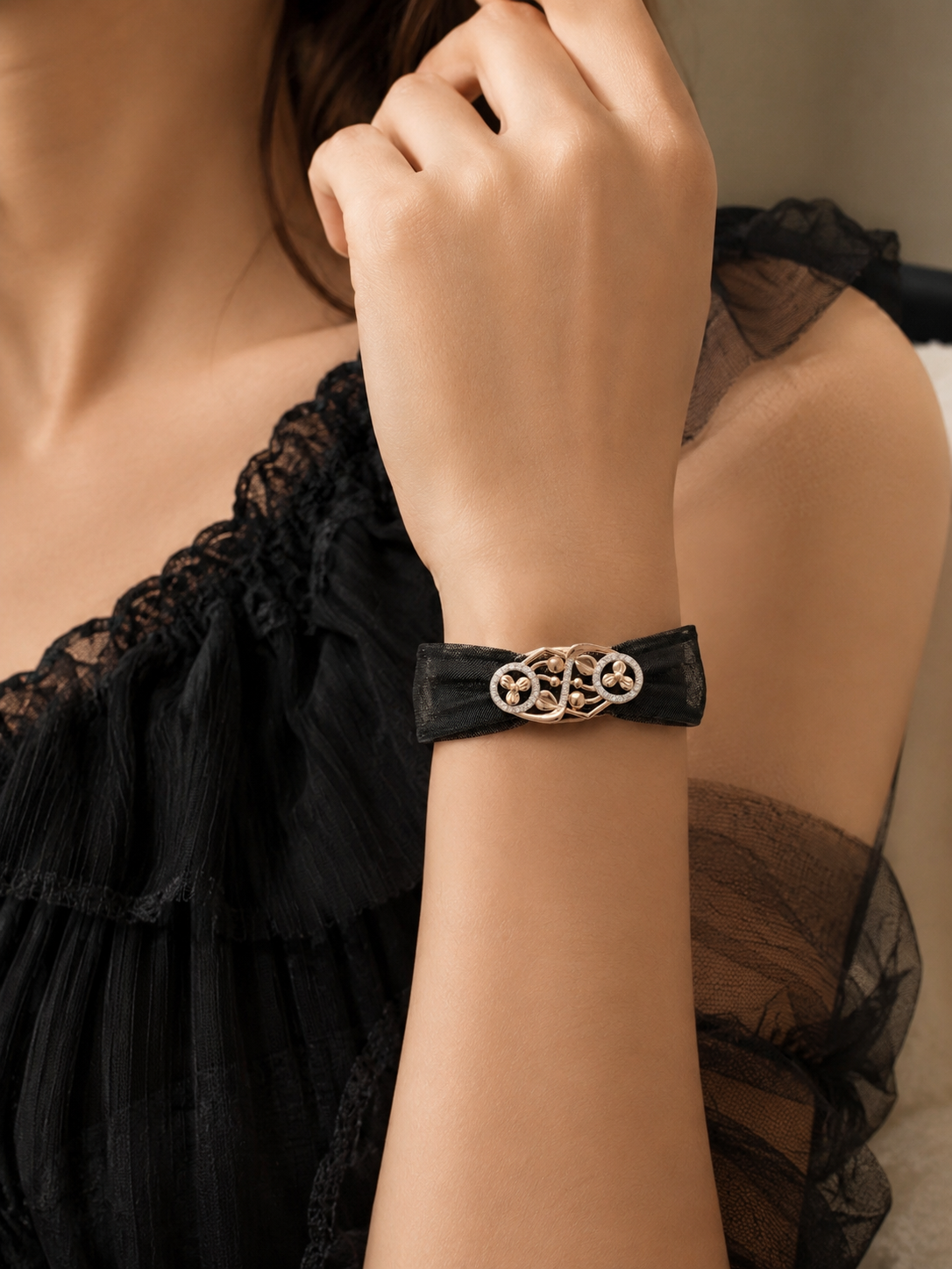 Black bracelet with a gold clasp on a wrist, worn by a person in a black lace garment.