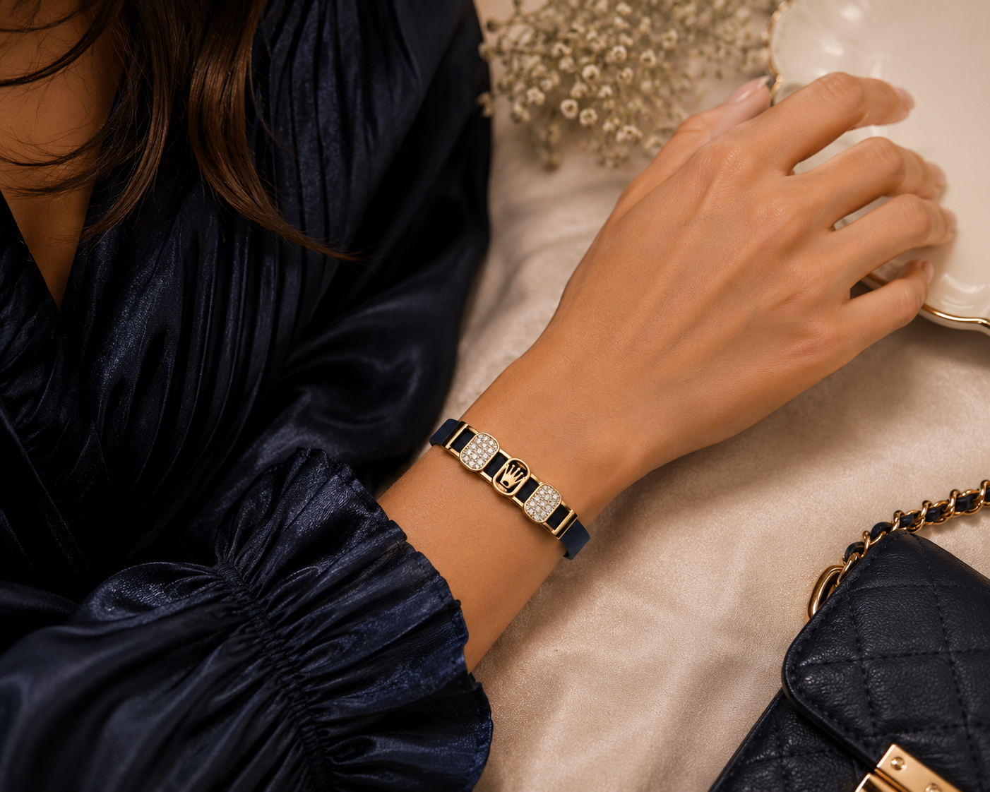 Woman's hand wearing a bracelet with a dark blue dress and handbag in the background