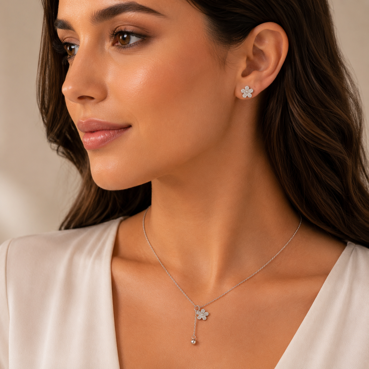 Woman wearing a silver necklace and earrings with a neutral background