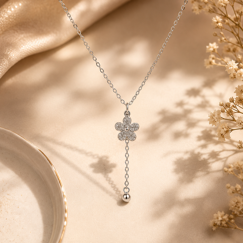 Silver necklace with a floral pendant on a beige surface with dried flowers.