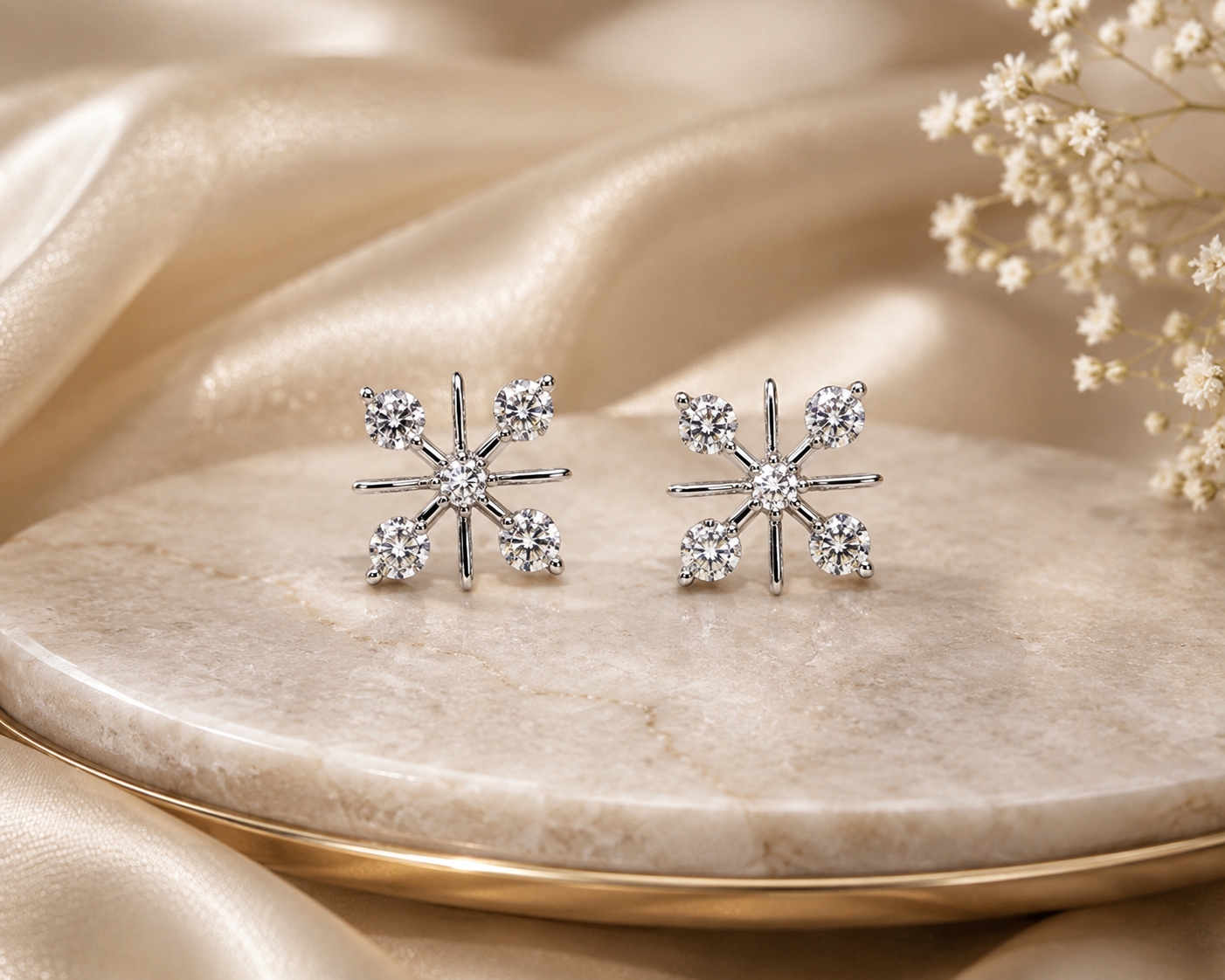 Silver snowflake earrings on a marble surface with beige fabric and flowers in the background
